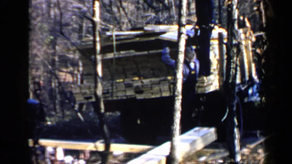 Home-movie frame from Birmingham, 1957, showing a man beside a lumber truck with planks and bare trees around him.