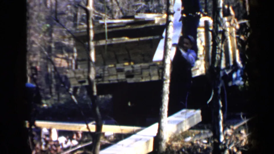 A worker in dark overalls handles a board near a lumber-loaded truck in the supplied 1957 Birmingham footage.
