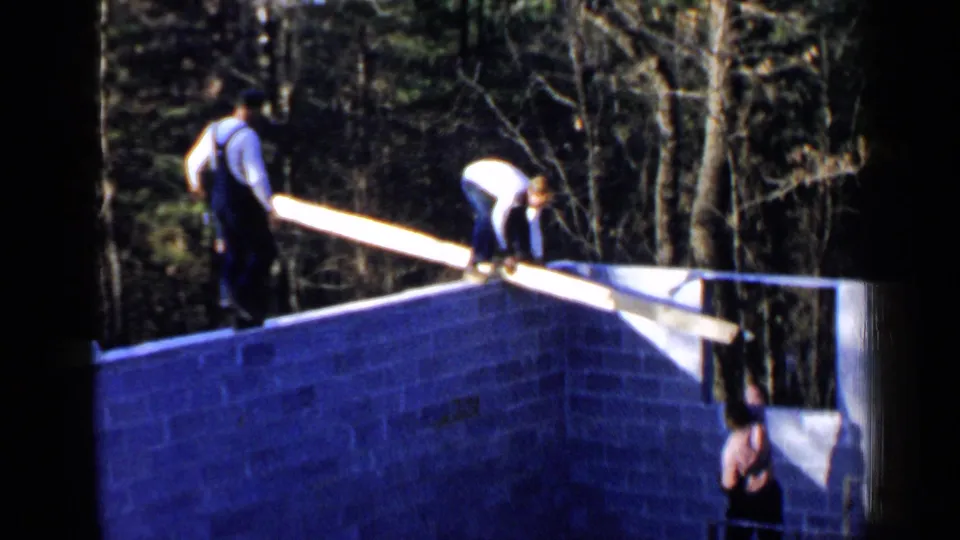 Two workers stand and bend on the cinder block foundation in Birmingham, Alabama, while a third man observes from the lower side.