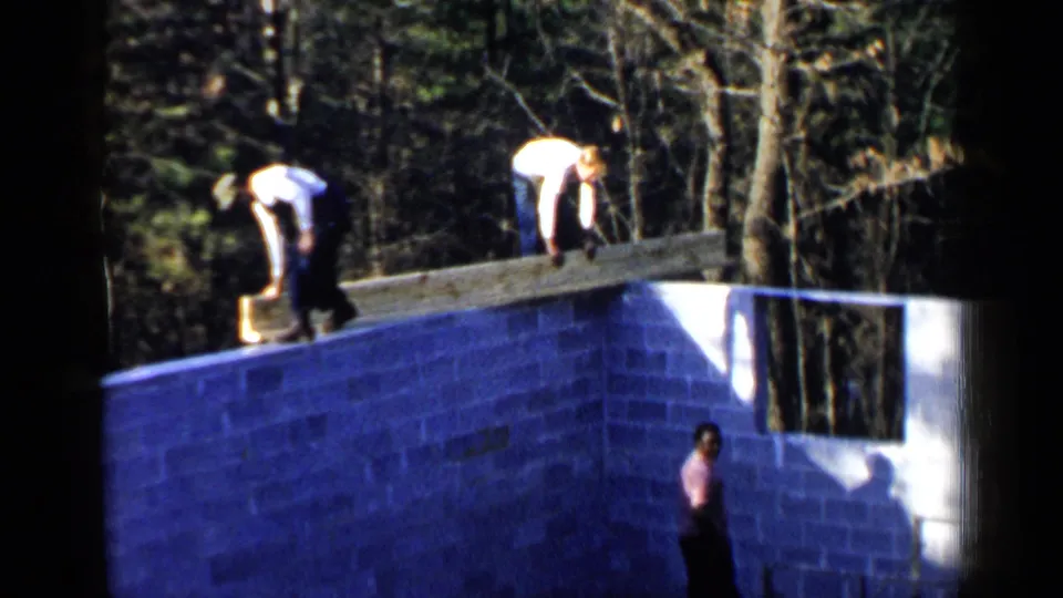 Men continue placing lumber on a cinder block foundation in Birmingham, Alabama, with a third figure visible below the wall.