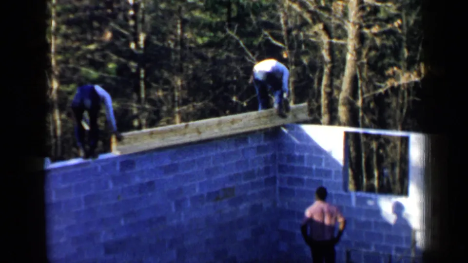 End frame of a 1957 Birmingham construction scene, with workers on a cinder block foundation and a man watching from below.
