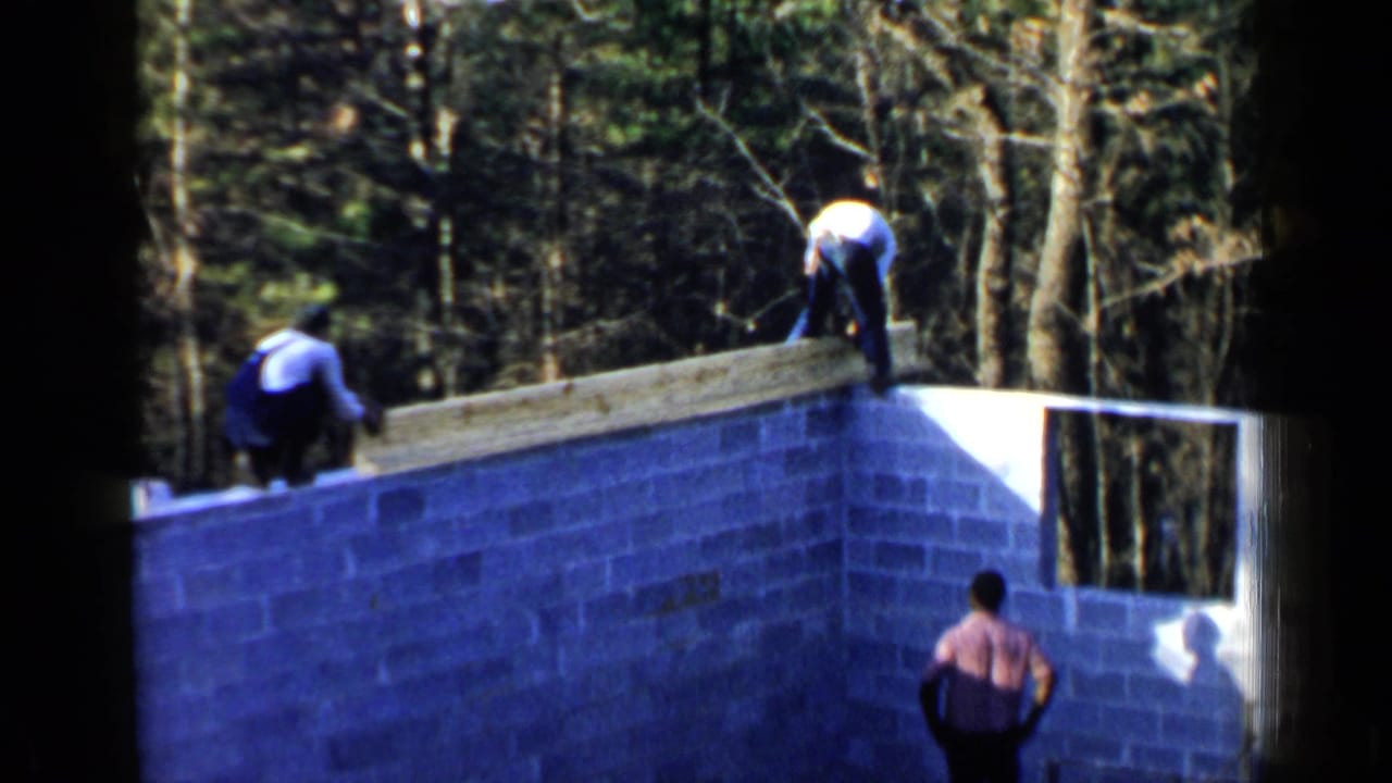 Workers on a cinder block foundation placing a long wooden beam near trees.