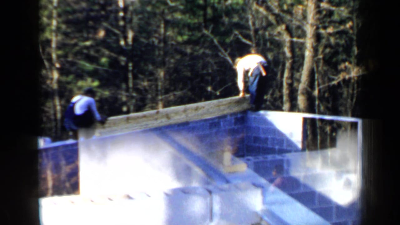 Men continue working along the top edge of an unfinished block wall.