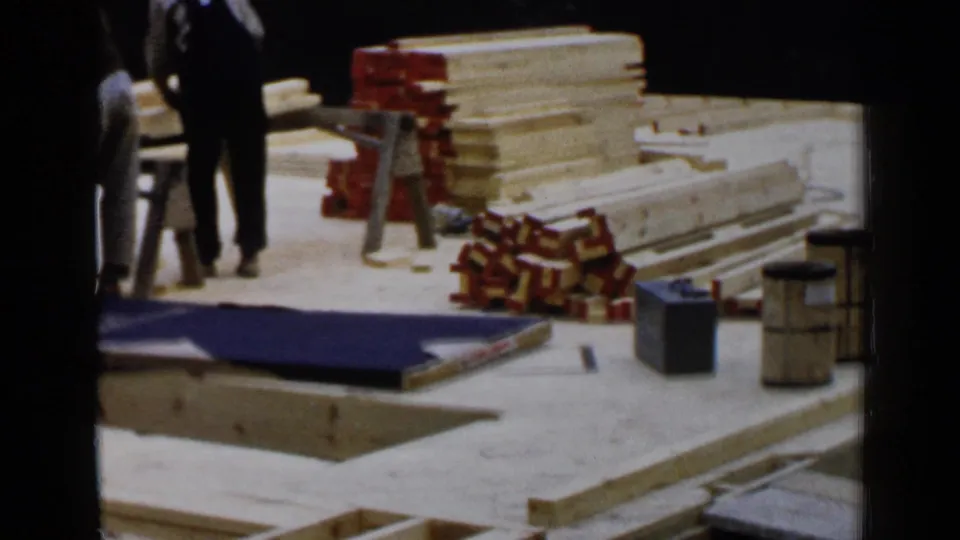 1957 Birmingham house-building footage shows workers near lumber piles, boxed materials, sawhorses, and scattered site supplies.
