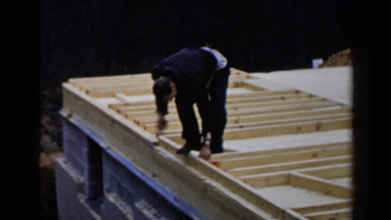 In Birmingham, Alabama in 1957, an adult man in dark clothing bends over exposed wooden roof beams on a partly built structure.