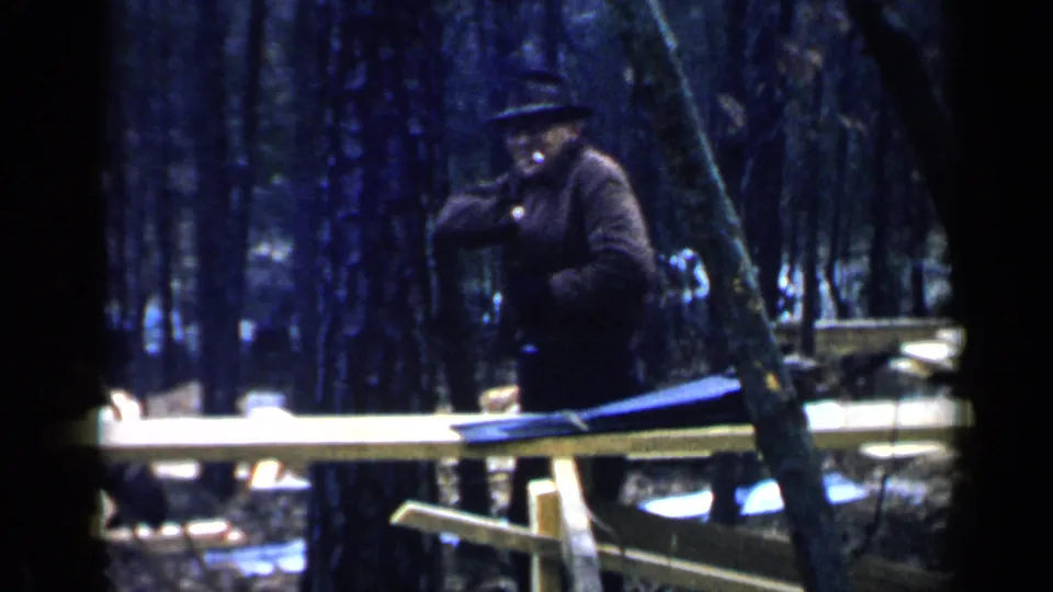 The man in a black hat and dark coat appears to reach into or adjust something at his inner coat pocket.