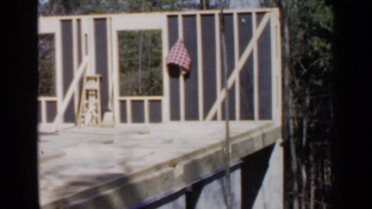Partially built house wall with open framing, tools on the floor, and trees behind it.