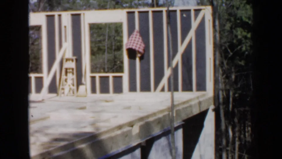 A Birmingham construction scene from 1957 shows open wall framing, a ladder, broom, checked cloth, and dense trees behind the structure.