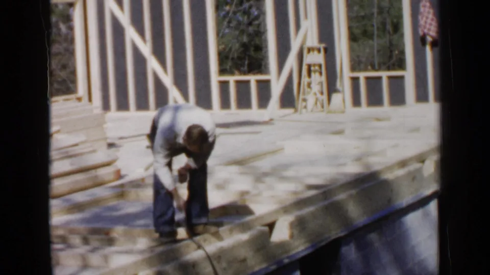 The final 1957 Birmingham frame shows the man still bent over the house framing, with exposed studs, window openings, and bright outdoor light.