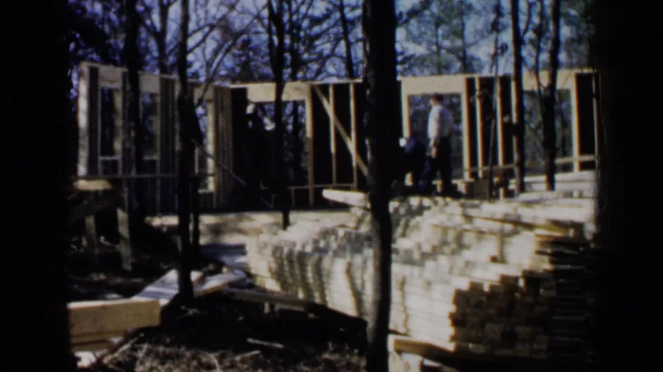 A wider 1957 Birmingham view shows workers on a raised wood frame, with stacked lumber, trees, and partial wall framing visible.