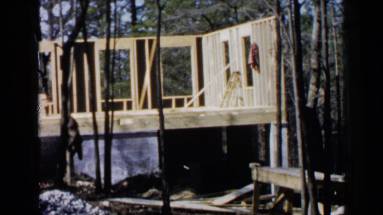 Wood-framed house under construction behind trees on a concrete foundation.