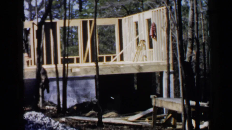 1957 Birmingham footage shows the same wooded construction site, with a ladder leaning near open framing and a red garment on the wall.