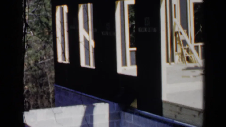 1957 Birmingham home-movie frame of unfinished house framing with open windows, pale lumber, and outdoor trees beyond.