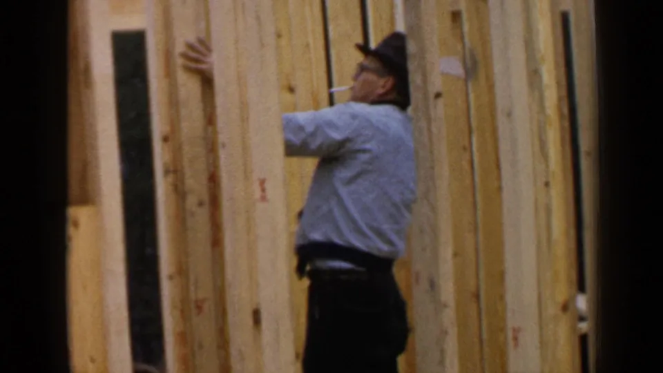 A carpenter in a light shirt and hat adjusts or steadies vertical lumber in the Birmingham construction scene.