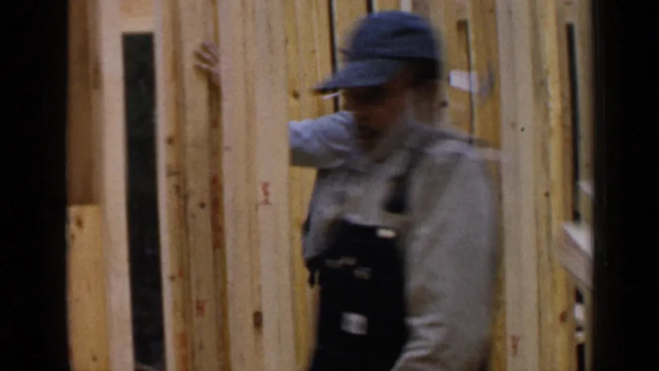 A capped worker moves across the foreground as another carpenter remains beside the raw wall framing in Birmingham.