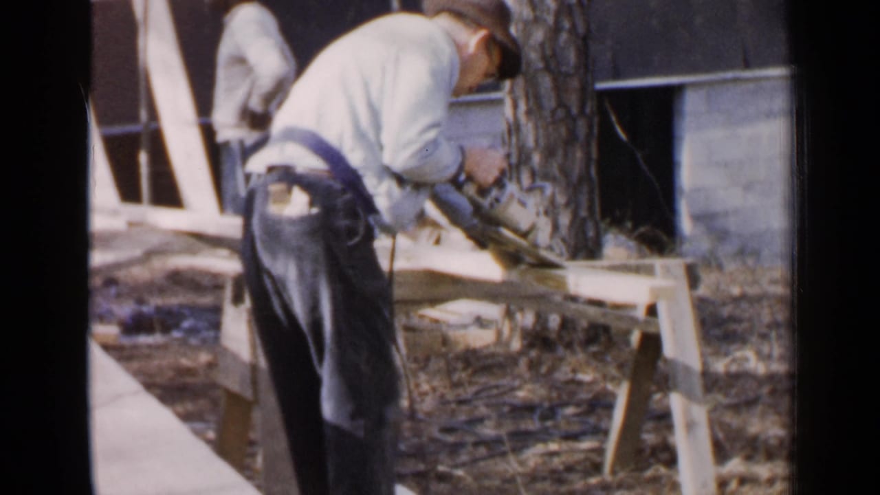 Man leans over a plank while handling a circular saw outdoors.