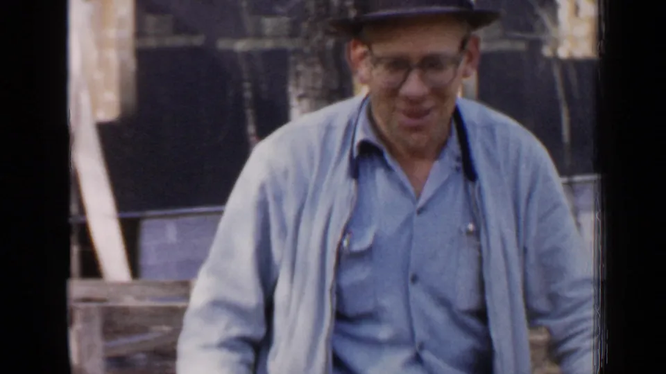 In the Birmingham home-movie footage, the man smiles toward the camera while standing by the outdoor woodworking setup.