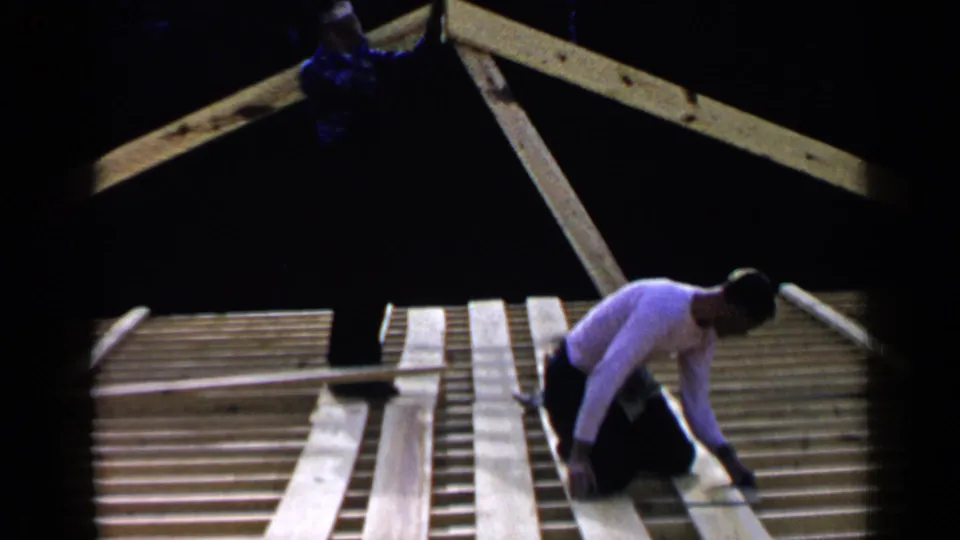 1957 Birmingham 8mm frame showing a man kneeling on roof framing and aligning a long board across the structure.