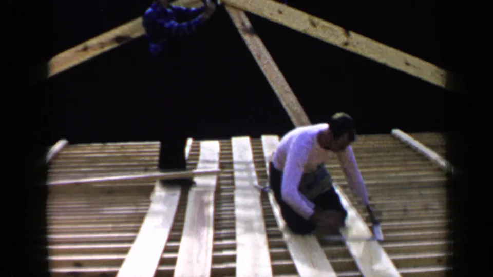 1957 Birmingham construction frame showing a worker bending over roof framing with multiple long boards in place.