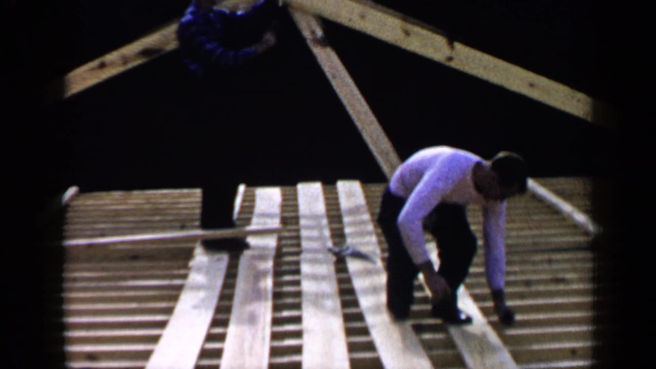 Man kneeling on exposed roof joists while placing long boards.