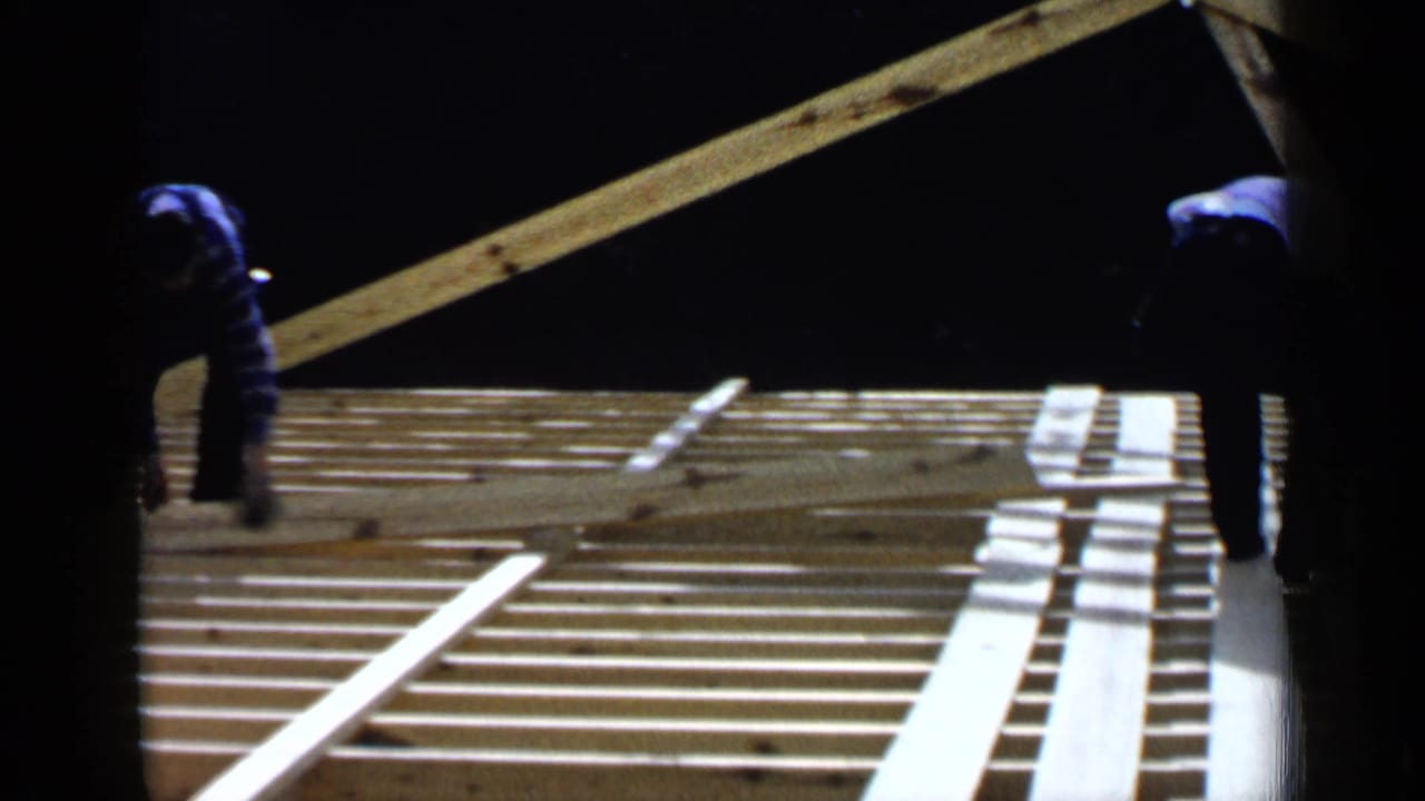 Silhouetted worker near roof joists and angled lumber under strong light.