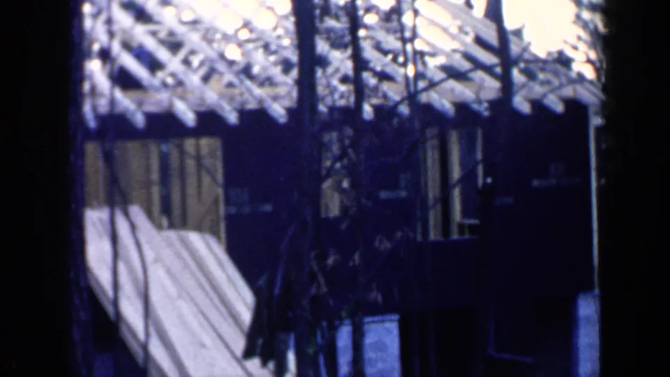 1957 Birmingham construction view with exposed roof framing, dark exterior walls, windows, trees, and pale lumber leaning against the building.