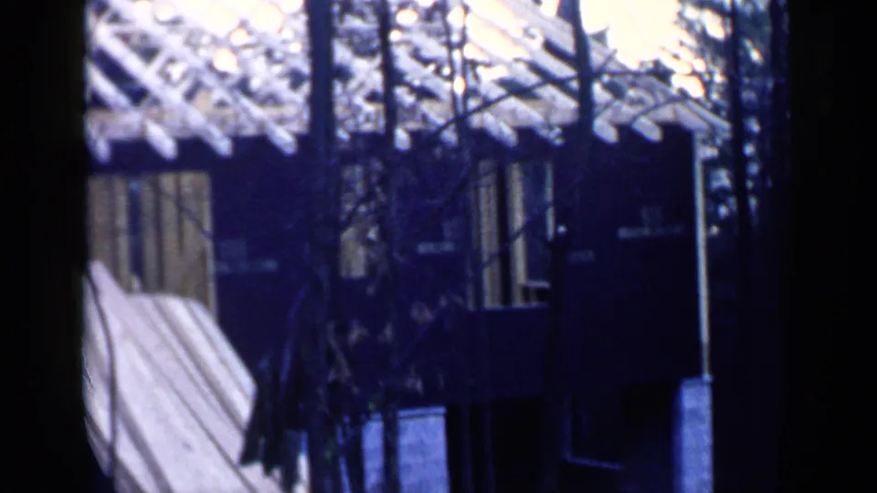 1957 Birmingham frame showing a partially built structure with windows, exposed trusses, leaning boards, and trees in the foreground.