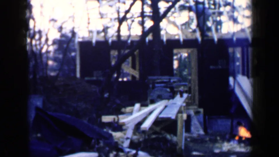 Birmingham, Alabama 1957 home-movie frame showing a partially built house structure, loose lumber, trees, and a small fire or bright orange light near the work area.