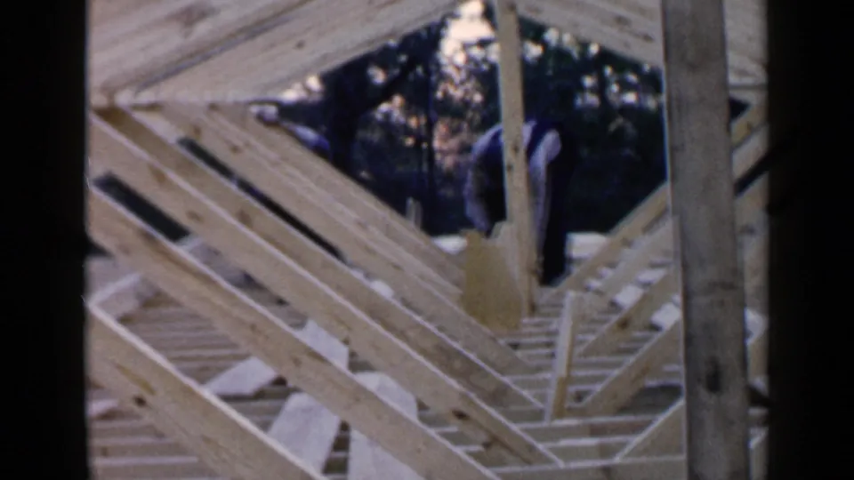 A man works among intersecting wooden rafters during a 1957 Birmingham residential construction scene.