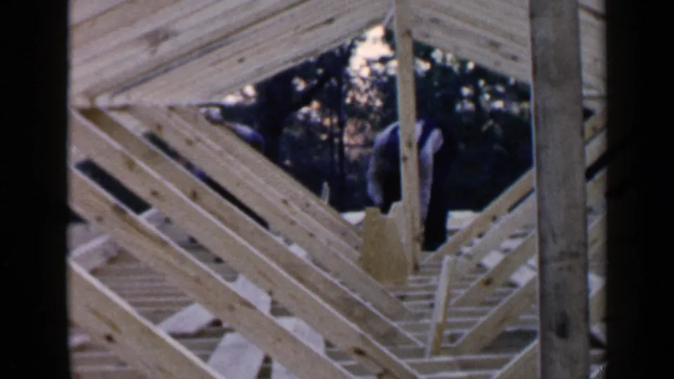 The home-movie frame shows a man in overalls using a hammer beside exposed rafters in Birmingham, Alabama, 1957.