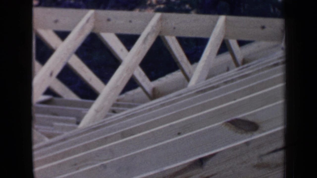 1957 Birmingham home-movie frame showing exposed wooden roof trusses, rafters, and laid boards during early house construction.
