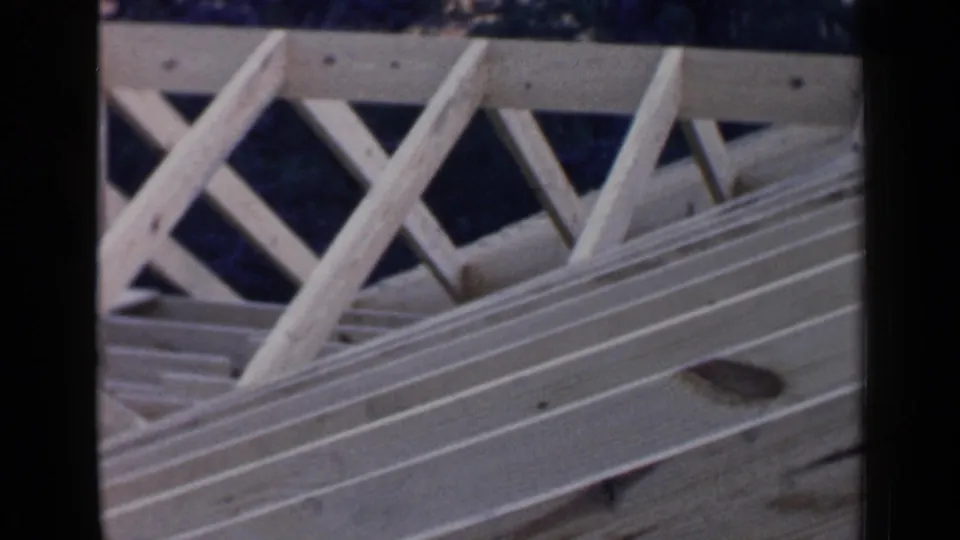 1957 Birmingham home-movie frame showing exposed wooden roof trusses, rafters, and laid boards during early house construction.