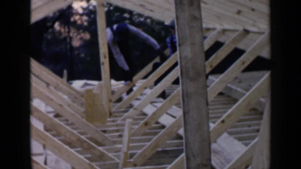 A worker in dark clothing appears on the unfinished roof frame of a 1957 Birmingham house construction scene.