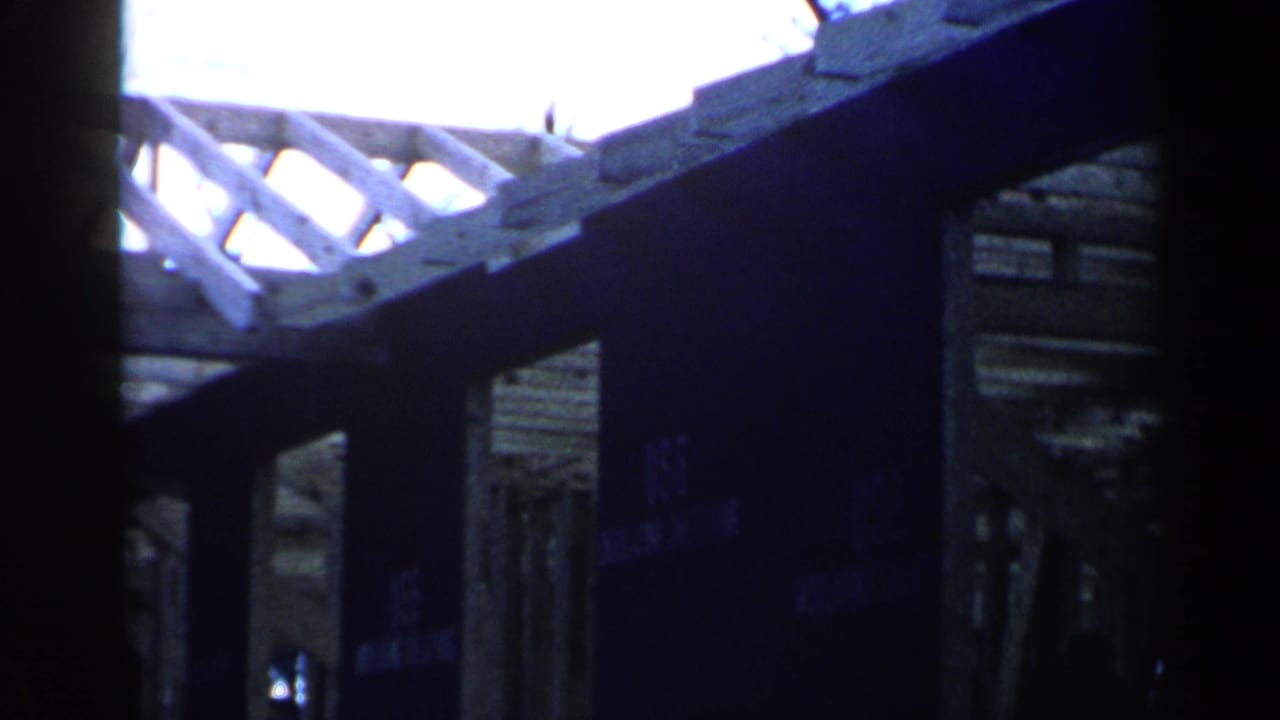 Interior view of a wooden building frame with rafters, beams, and dark vertical supports.