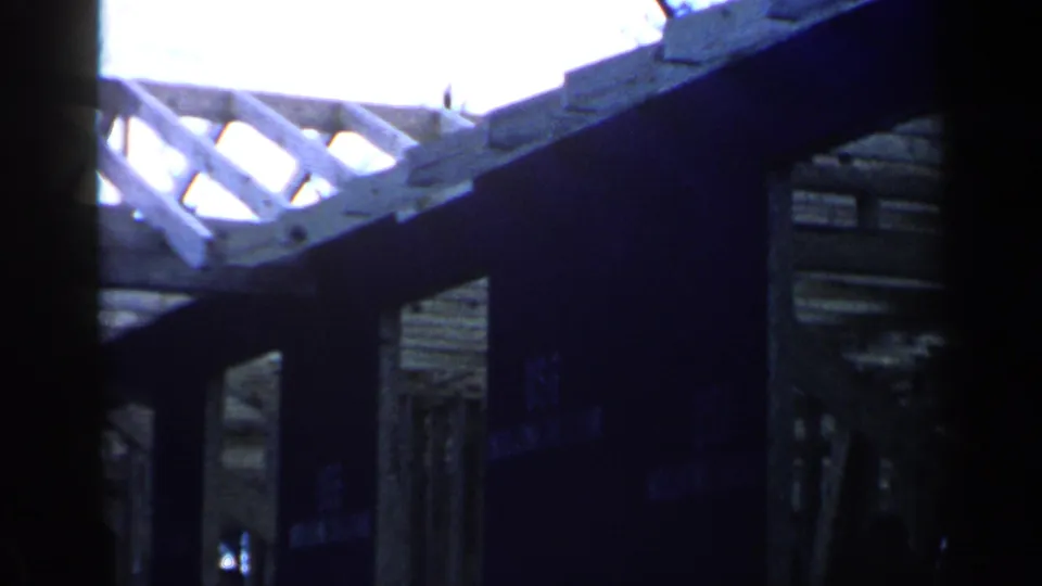 1957 Birmingham home-movie frame showing exposed rafters and dark structural supports inside an unfinished wooden structure.