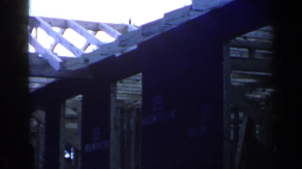 1957 Birmingham footage shows a dim interior framing view with rafters, beams, and daylight beyond the unfinished structure.