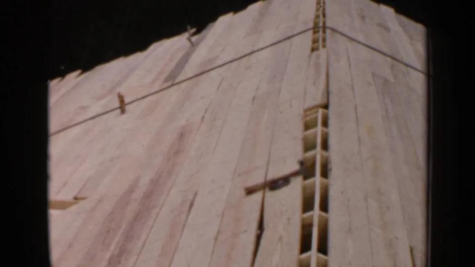 Close view of a sloped unfinished wooden surface in 1957 Birmingham footage, with seams, a narrow opening, and small projecting pieces.