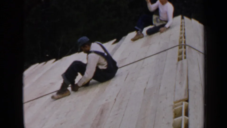 The final frame shows two men seated on an unfinished wooden roof in Birmingham, Alabama, with trees behind the construction area.