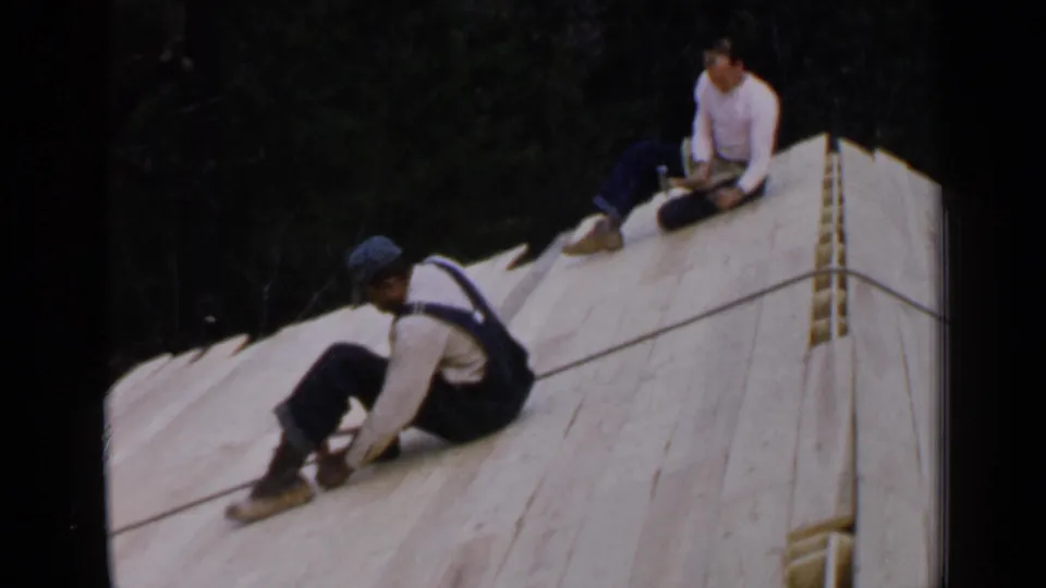 Birmingham, Alabama, 1957 home-movie frame of two workers on a pale wooden roof deck with trees behind them.