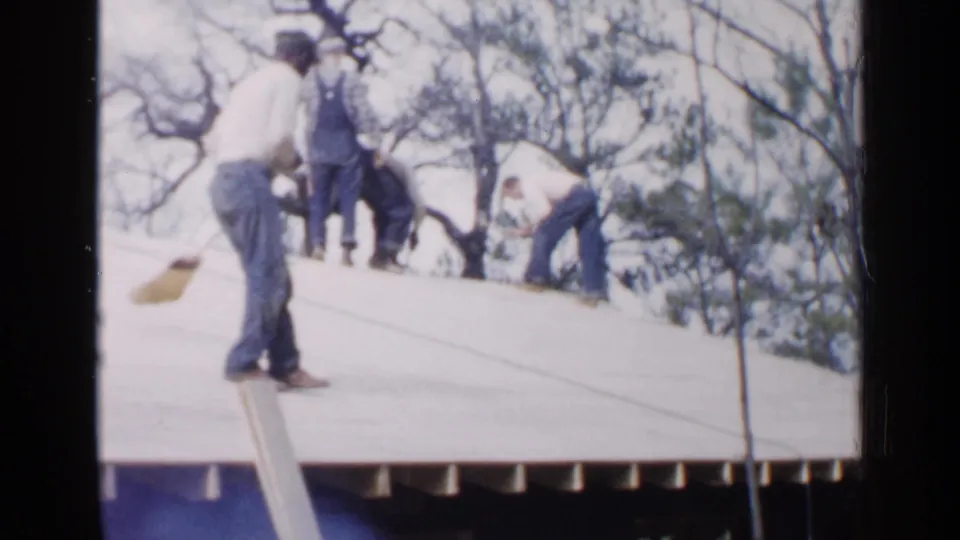 Birmingham, Alabama, 1957 frame of a man holding a broom on a roof as other workers continue roofing tasks in the background.