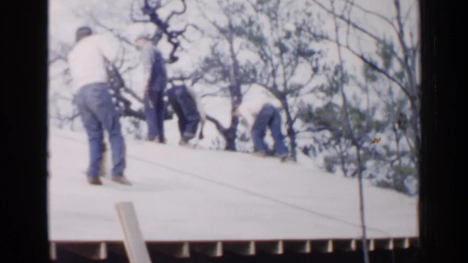 Men in casual work clothes sweep and bend across a sloped roof in archival 1957 Birmingham footage.