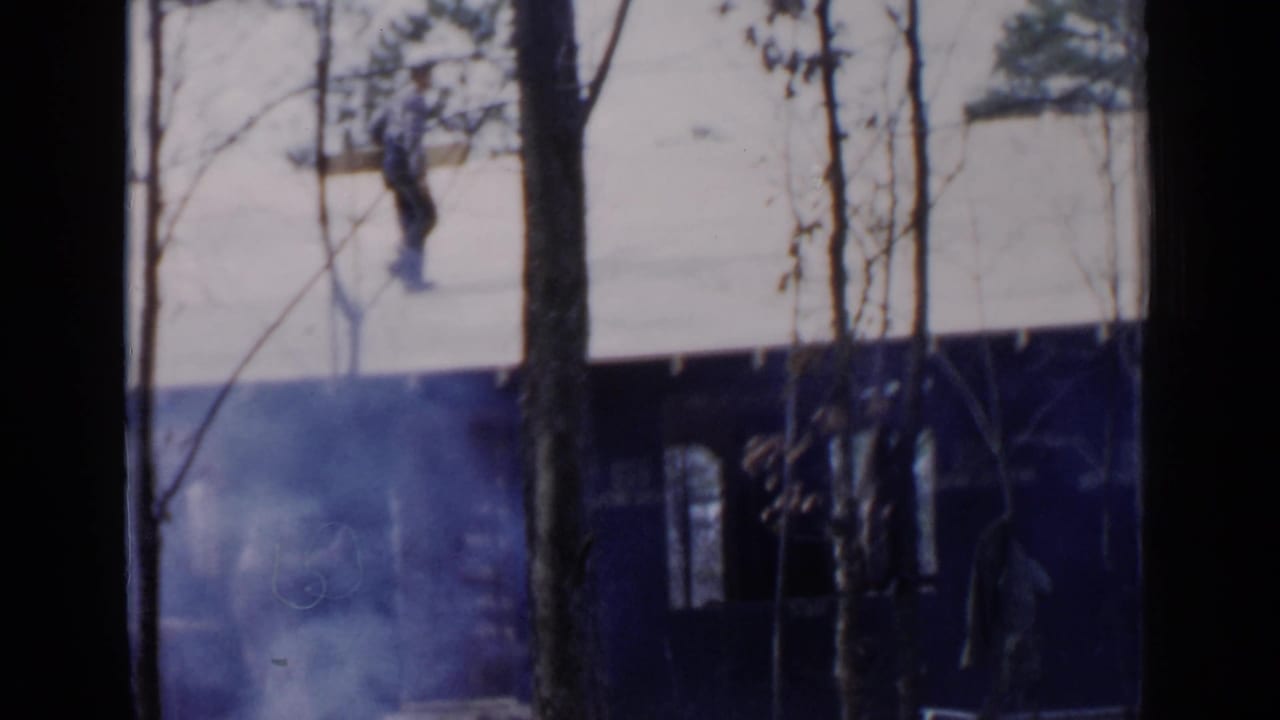 1957 Birmingham 8mm frame showing a distant figure crossing a snow-covered roof through winter trees.