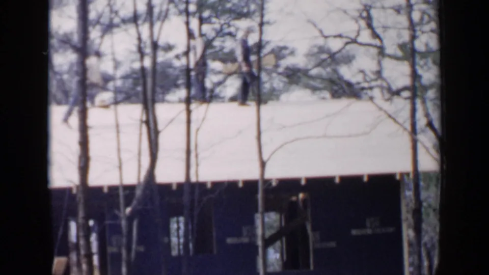A distant worker appears near the roof edge of a Birmingham construction scene, with trees and dark frame edges obscuring the view.