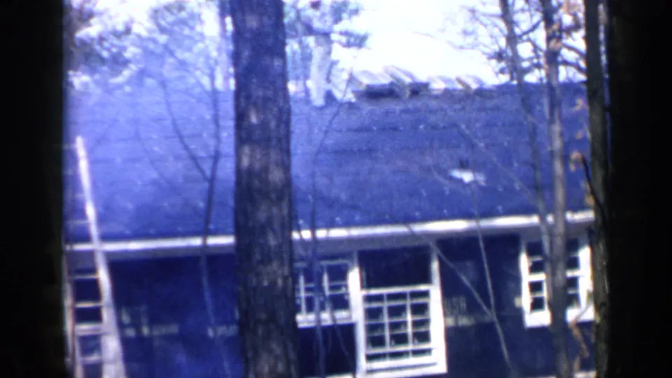 1957 Birmingham frame showing the dark roof, white-trimmed windows, and tree trunks in front of the house.