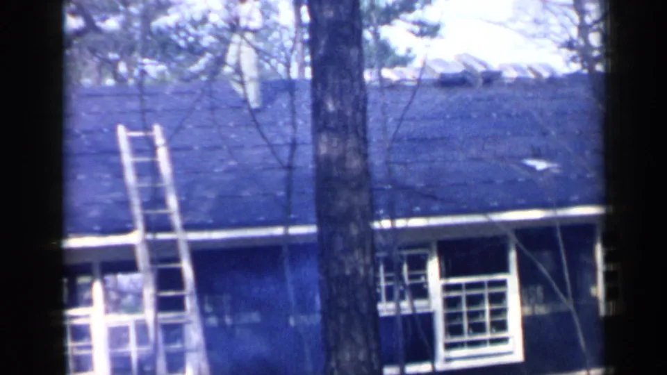 A wooden ladder stands against the dark-roofed house, seen through bare trees in the 1957 Birmingham home-movie footage.