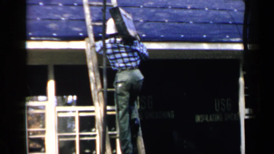 The man continues upward on the ladder with the dark panel beside the blue shingled roof in Birmingham, Alabama, 1957.
