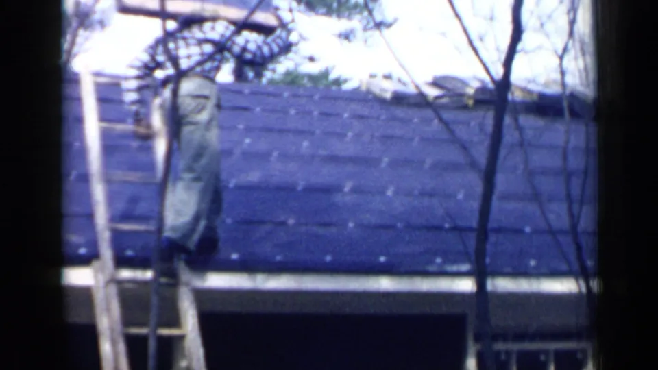 In Birmingham, Alabama, 1957, a man in light pants climbs a ladder to a shingled roof while carrying roofing supplies.