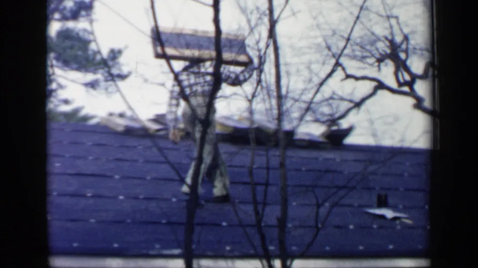 A man appears to work or place material on the roof, with bare tree branches partly obscuring the 1957 Birmingham scene.