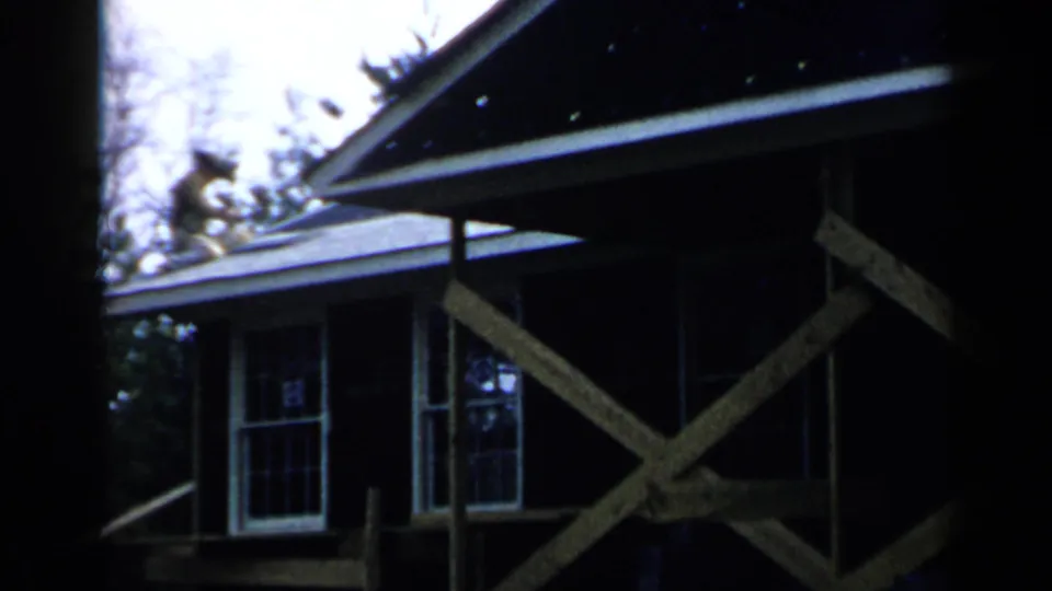 A man works near the roofline above wooden scaffolding on a residential exterior in Birmingham, Alabama, 1957.