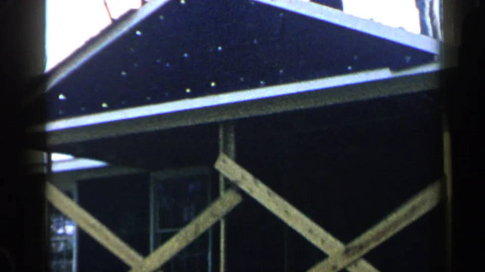1957 Birmingham frame focused on the house structure, roof overhang, white-trimmed window, and diagonal wood bracing.